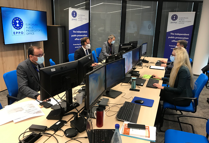 four men and one woman sitting at desk behind screens