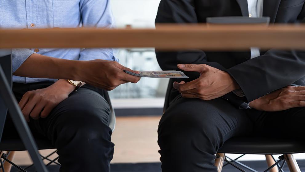 someone handing money to someone else underneath a table